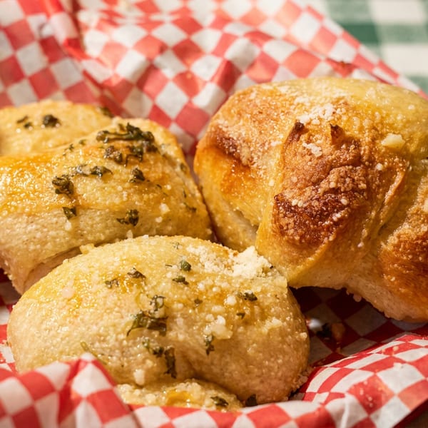 Golden-brown garlic knots topped with parmesan and herbs in a red checkered basket.